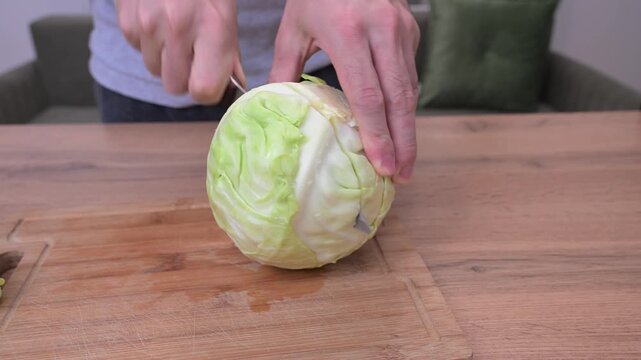 Skilled hands precisely halving and slicing fresh green cabbage on rustic wooden cutting board during meal preparation