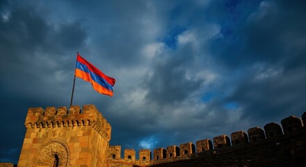 armenian flag waving atop historic stone fortress against dramatic cloudy sky. cultural heritage and pride. travel, history. armenia national day