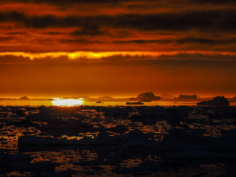 Vibrant Arctic sunset with fiery red sky reflecting over frozen sea and drifting icebergs.
