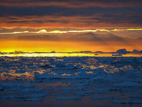 Vibrant Arctic sunset with fiery red sky reflecting over frozen sea and drifting icebergs.