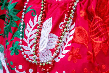 A red and green embroidered blouse with a white background. The blouse has a green and white flower...