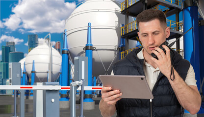 Engineer with tablet and radio inspects gas storage tanks, ensuring safety and industrial operations. Activity: Oil, Gas, Energy, Industry.