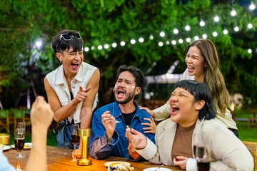 Group of Happy Asian people diverse friends enjoy and fun celebration meeting social gathering dinner party eating cake, drinking wine and talking together in the garden at restaurant in evening.