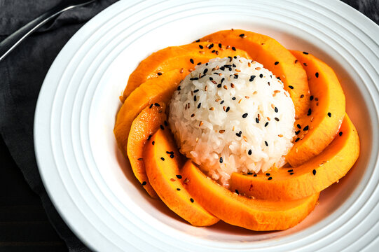 Mango Sticky Rice Drizzled with Coconut Sauce in a Shallow Bowl Close-up: Thai dessert with glutinous rice, fresh fruit, and toasted sesame seeds