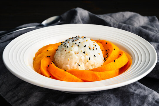 Mango Sticky Rice Drizzled with Coconut Sauce in a Shallow Bowl Side View: Thai dessert with glutinous rice, fresh fruit, and toasted sesame seeds