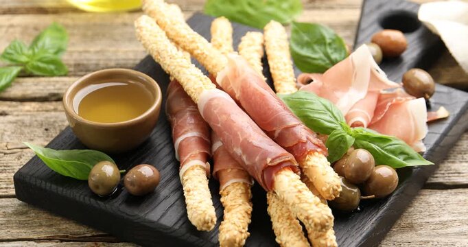 Grissini breadsticks with prosciutto, olives and honey on wooden table, spinning