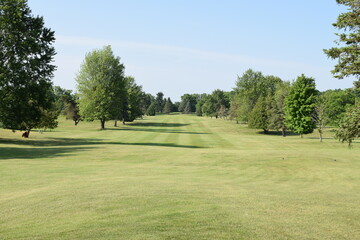 Looking down a tree lined golf course fairway towards the putting green.