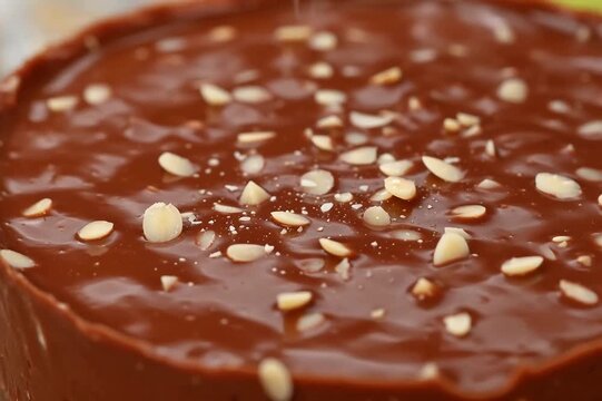 Final finishing touch as a baker sprinkles chopped nuts over a decadent chocolate ganache dessert
