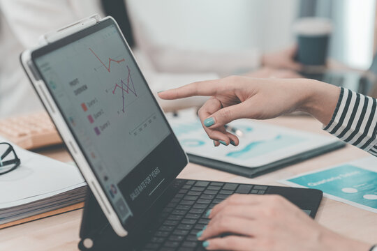Two businesswomen having a meeting and looking at financial data, charts and graphs on a digital tablet. Business consultant analyzing financial figures.