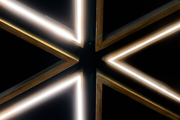 Abstract geometric ceiling light design with glowing LED strips in wooden frames forming symmetrical triangular patterns on a dark background.
