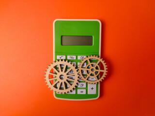 The image displays a green calculator accompanied by two wooden gears on an orange background