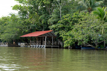 Obraz premium Wooden house on stilts by the riverside surrounded by trees.