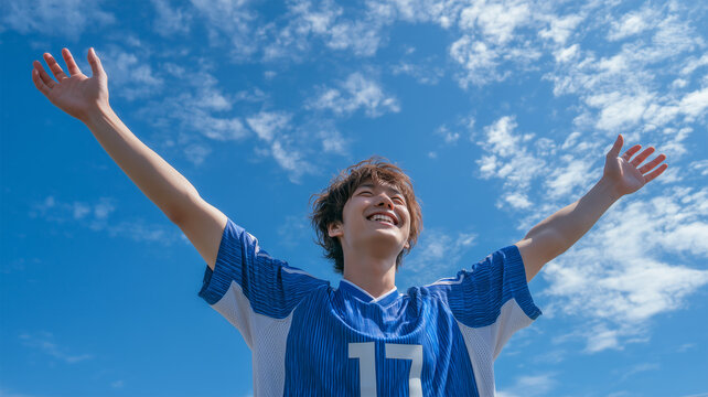 男の子がサッカーのユニフォーム姿で青空に伸びをする