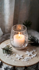 White candle in frosted glass holder on birchwood table with pine needles and holly berries, winter holiday decor, concept of Christmas