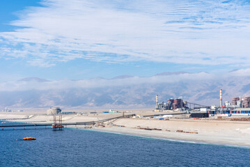 Fototapeta premium Industrial zone in Mejillones, Puerto Angamos, Chile, near the Atacama Desert. Features include industrial structures with smokestacks along a sandy coastline.