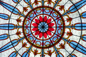 Intricate stained glass ceiling with a symmetrical floral design in red, blue, yellow, and white, forming a circular mandala-like pattern.