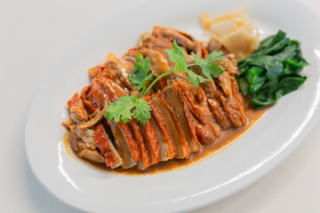 Roasted duck with rich brown sauce served on a white plate, garnished with fresh cilantro, vegetables, and pickled ginger. Asian Food culture.
