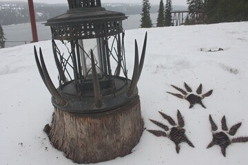 Ornate metal lantern on a stump, animal tracks in snow