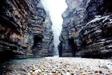 Steep, rocky canyon walls meet in a narrow passage, a riverbed filled with stones and snow