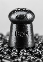 A close-up view of a dark gray metal cap or stopper, resting on a bed of small, dark gray metal beads.