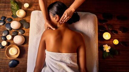 A young woman lying face down on a massage bed, a therapist giving a back massage under warm candlelight, soft golden glow, cozy spa atmosphere, wooden floor and natural stone walls, calm expression o