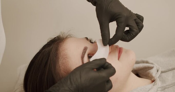 Master combing woman's eyelashes after lamination. Beautiful young woman with eyelash extension. Woman eye with long eyelashes. Beautician eyelash extension for young woman in a beauty salon