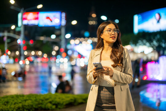 Young businesswoman using smartphone in a busy city at night
