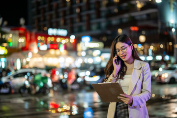 Businesswoman using smartphone and holding clipboard in night city