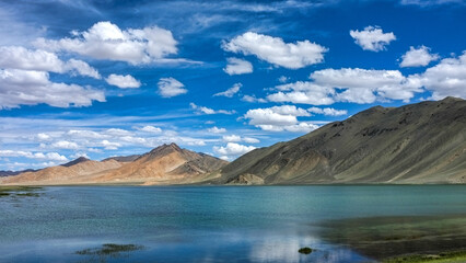 Snow-capped peaks reflect in a tranquil mountain lake under a cloudy sky