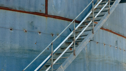 A metal staircase rises against an aged blue structure, showing signs of wear. This scene captures...