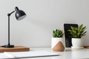 Minimalist modern home office desk setup with two potted plants smart device and lamp on clean white surface against plain gray wall background