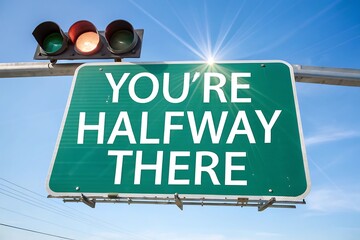 Bright green highway sign reads you're halfway there against blue sky traffic light