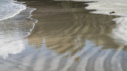 Ocean waves are spreading across the sandy beach. Delicate foam, wavy pattern, reflection on wet smooth sand. Close-up. Malaysia. Borneo. Kota Kinabalu.