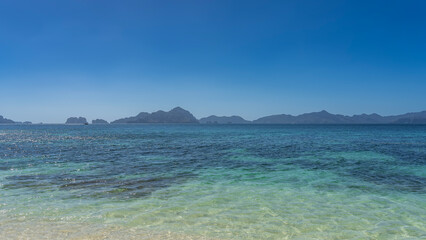 Fototapeta premium Minimalistic seascape. A calm crystal clear aquamarine turquoise ocean. Mountains on the horizon. Clear blue sky. Copy space. Philippines. Palawan.
