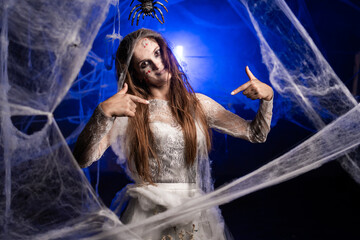 Sinister woman with horrible Halloween zombie makeup pointing fingers on herself while standing on...