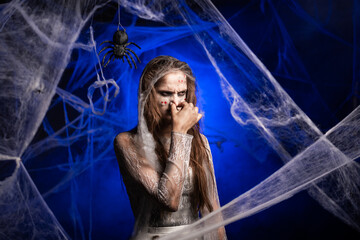 Sinister woman with horrible scary Halloween zombie makeup in white dress pinching nose with...