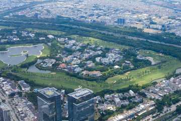 Obraz premium Aerial view of a large green golf course surrounded by residential areas and city buildings, showing a contrast between urban life and natural landscape with lakes, roads, and trees.
