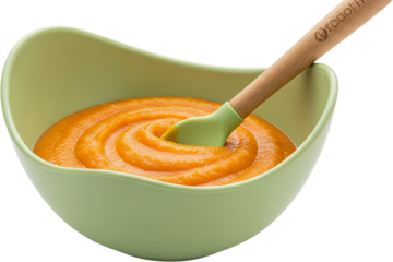 Bright orange puree swirled in a pastel green bowl with a light wood spoon and silicone spatula isolate