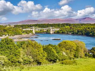 Fototapeta premium Menai Suspension Bridge, the lush green spring landscape of Anglesey, and the mountains of Snowdonia as a backdrop. North Wales, UK.