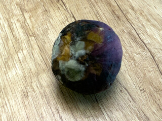 Close-up of rotten fig with mold on wooden table, spoiled fruit showing decay, fungus contamination and food waste, unhealthy and inedible produce.