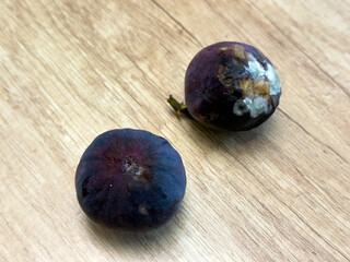 Two rotten figs with mold on wooden table, spoiled purple fruits showing decay and fungus...