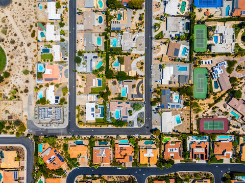 Aerial view of an upscale residential neighborhood with red-tiled roofs, palm trees, and private swimming pools in Palm Springs, California. 