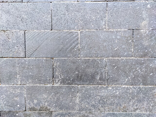 A textured, close-up shot of a modern wall composed of rough, dark gray rectangular stone blocks. The natural variations and subtle specks of white highlight the rugged, industrial.