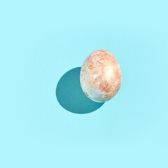 Single speckled egg casting shadow on vibrant light blue background.