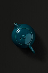 Green ceramic teapot with lid and spout, viewed from above on a dark textured background