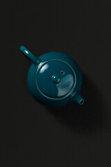 Green ceramic teapot with lid and spout, viewed from above on a dark textured background