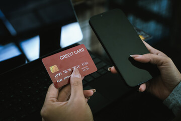 Close-up of hands holding a credit card and smartphone with a laptop and coffee cup in the background, symbolizing online payment.