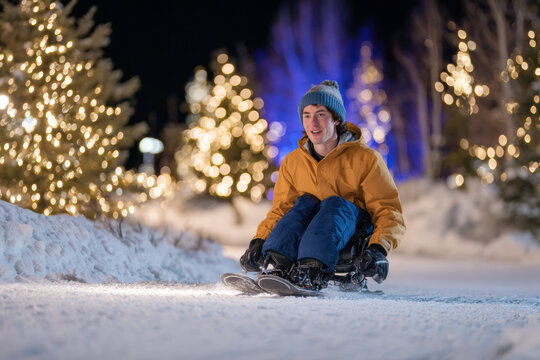 Joyful person in an adaptive ski enjoying snowy winter night with festive lights. happy disabled athlete enjoying an accessible sport and active holiday lifestyle