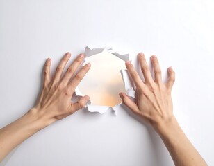 Hands tearing a hole in white paper, revealing a soft, pastel sky