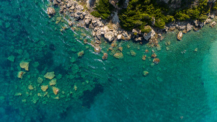 Aerial top view of rocky shoreline with crystal clear turquoise water showing submerged stones and green coastal cliffs Zakynthos Greece